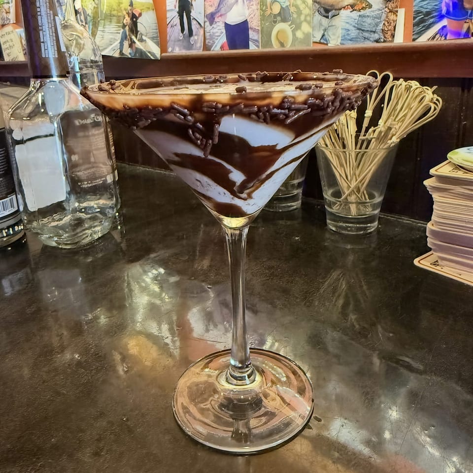 Martini glass dessert with chocolate drizzle and sprinkles on a bar counter.