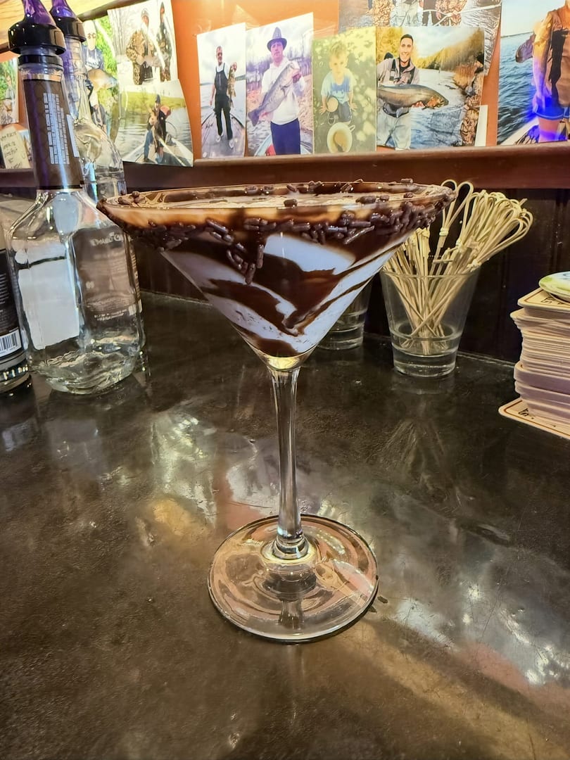 Martini glass dessert with chocolate drizzle and sprinkles on a bar counter.